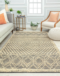 Bright living room with a geometric patterned rug, gray sofa, modern armchair, side table, and plants, creating a fresh and inviting space