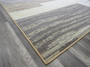 Edge view of modern abstract rug, featuring geometric patterns in brown and beige, displayed on a wooden floor for contemporary decor.