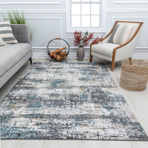 Cozy living room with a grey sofa, a white armchair, a rustic firewood holder, a blue and grey abstract rug, and decorative plants.