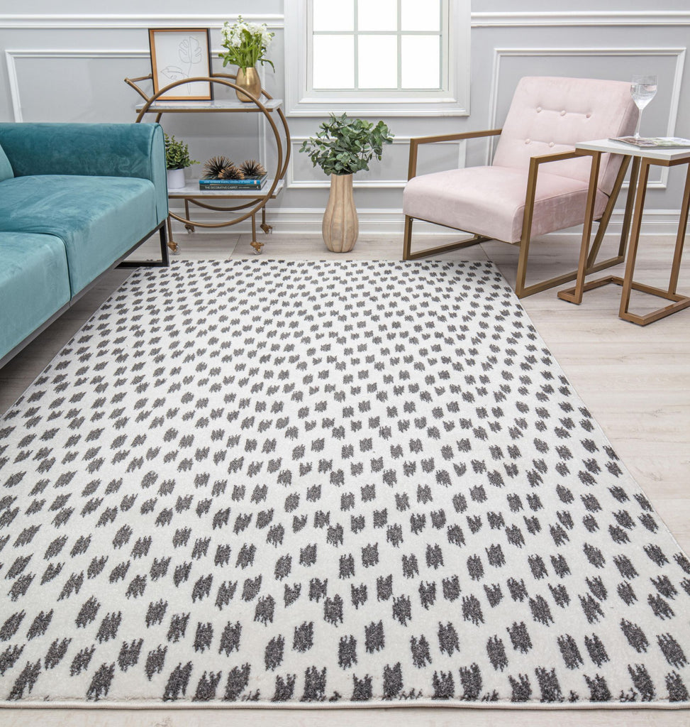 Modern living room featuring a geometric patterned rug in black and white, with a teal sofa, beige armchair, and decorative accents.