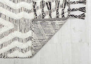 Close-up of the corner of a white and black striped rug with tassels.