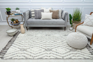 Modern living room with a gray sofa, decorative pillows, plants, and a white and black geometric pattern rug.