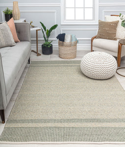 Modern living room with a gray sofa, striped beige rug, wooden armchair, knitted pouf, potted plant, and woven basket