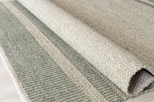 Close-up of a green woven rug rolled up, showcasing the detailed texture and craftsmanship, perfect for modern home decor.