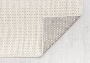 Close-up of beige woven rug with a flipped corner, displaying the detailed texture and quality of both the front and backing.