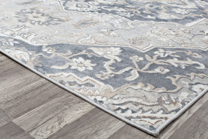 Corner view of a gray and white traditional pattern rug on a wooden floor.