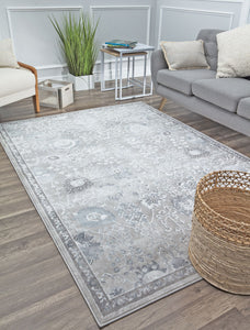 Elegant grey rug in a modern living room, featuring a grey sofa with cream pillows, a wooden chair, a plant, and a wicker basket