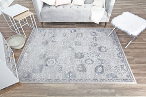 Top view of a gray patterned area rug in a cozy living room setting, featuring a sofa, side table, and wooden flooring.