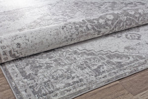 Close-up of a rolled gray vintage rug with distressed patterns, highlighting its texture and intricate design on a wooden floor.