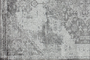 Close-up of a gray vintage rug with intricate distressed patterns, showcasing its detailed design and texture on a wooden floor.