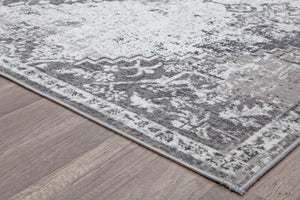 Corner view of a gray and white vintage rug on hardwood floor, showcasing the intricate border pattern and texture.