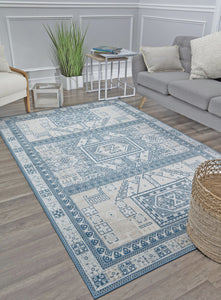 Stylish living room with a gray sofa, geometric blue and white rug, wooden floor, side tables, green plant, and woven basket