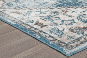 Corner view of a blue and gray distressed rug on a wooden floor, showcasing its detailed edge and vintage-inspired pattern.