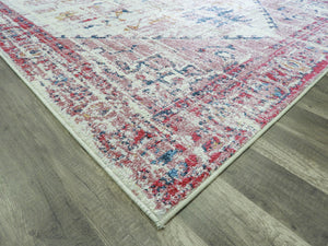 Corner view of an antique rose area rug with intricate patterns on a wooden floor.