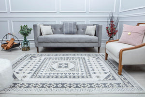 Living room with a grey sofa and armchair featuring an elegant white and grey patterned area rug.