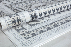 Close-up of a white and grey patterned area rug, rolled partially to show design details.