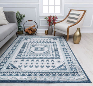 Blue and white geometric patterned rug in a modern living room with a chair, sofa, and decorative plants and vases.