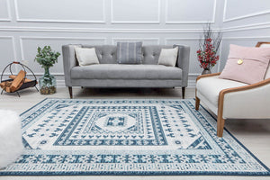 Elegant living room with a grey sofa, a white armchair, a blue and white patterned rug, a rustic firewood holder, and decorative plants