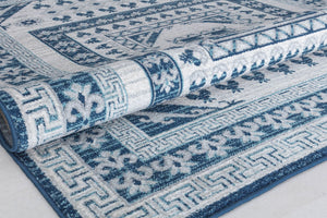 Close-up of a rolled blue and white geometric patterned rug showcasing intricate floral and border details.