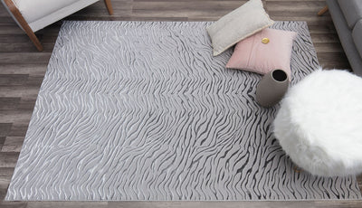 Top view of a white textured rug with wave-like patterns in a cozy living room setting with pillows and decor items.