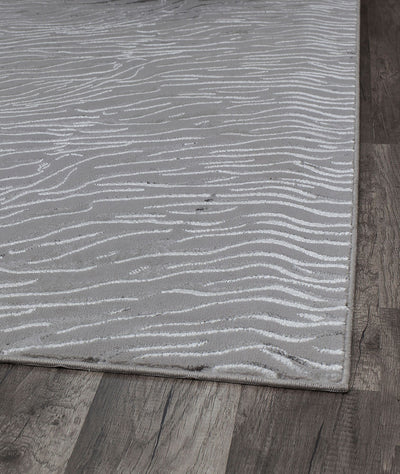 Close-up of the corner of a white textured rug with wave-like patterns on wooden flooring.