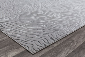 Close-up of the edge of a white textured rug with a wave-like pattern on wooden flooring.