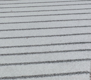 Close-up of a modern rug with black horizontal lines on a white background, showcasing its minimalist design and texture.