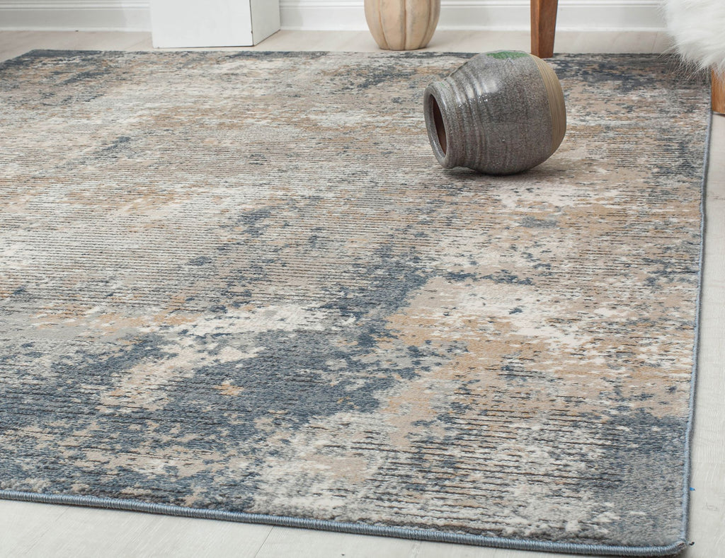 Close-up of a distressed blue and beige abstract rug with a decorative vase in a modern living room setting.