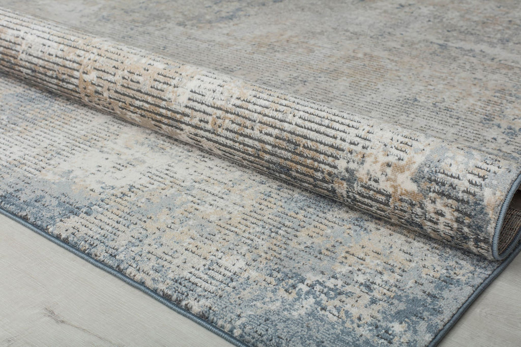 Close-up of a rolled distressed blue and beige abstract rug showing its detailed texture and pattern.