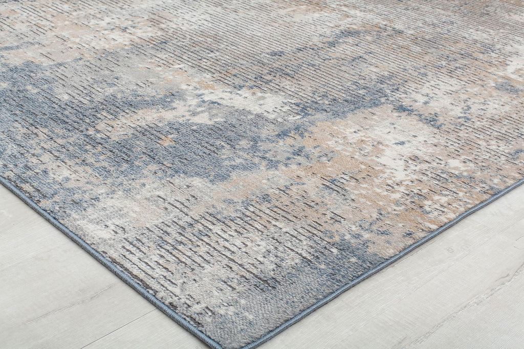 Close-up of a distressed blue and beige abstract rug's corner, showcasing its textured pattern and detailed design.