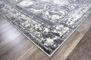 Corner of an abstract rug on a wooden floor, highlighting the intricate gray and white design.