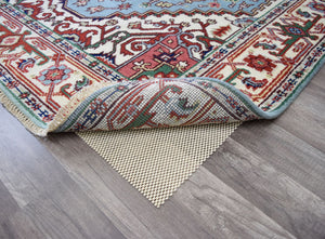 Corner of a blue and red traditional area rug, slightly rolled to show the non-slip pad underneath.