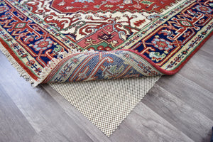 Corner of a vibrant red and blue area rug, slightly rolled to show the non-slip pad underneath.