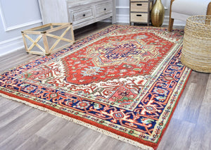 Traditional living room with a vibrant red and blue Persian rug, rustic furniture, a wicker basket, and a gold vase for decor.