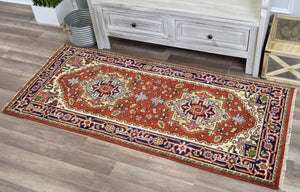 Red and blue area rug with traditional designs placed in front of a rustic cabinet.