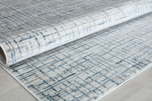 Close-up of a blue and gray geometric area rug rolled up, showcasing its detailed pattern and soft texture.