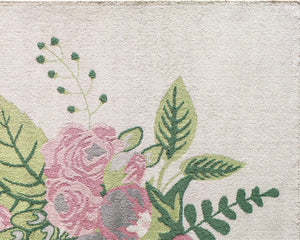 Close-up of floral rug design featuring pink roses and green leaves on a cream background, showcasing intricate detailing and texture.