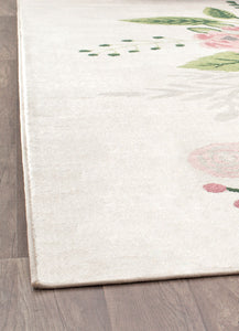 Edge of a floral rug on a wooden floor, featuring a delicate cream background with subtle green and pink leaf patterns.