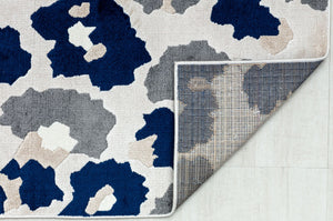 Underside view of a blue and gray floral patterned rug showing its backing and abstract flower designs.