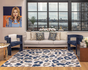 Stylish living room with large windows, navy blue chairs, white sofa, colorful art, and blue and beige patterned rug overlooking cityscape