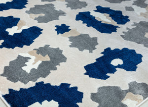 Close-up of the corner of a blue and gray floral patterned rug with abstract flower designs, showcasing its detailed texture.