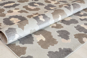 Close-up of a rolled beige and gray floral patterned rug highlighting its abstract flower designs.