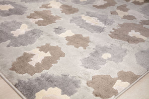 Close-up of the corner of a beige and gray floral patterned rug with abstract flower designs.