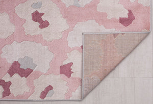 Underside view of a pink and beige floral patterned rug showing its backing and abstract flower designs.