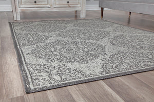 Side view of a grey area rug with intricate floral patterns on a wooden floor.