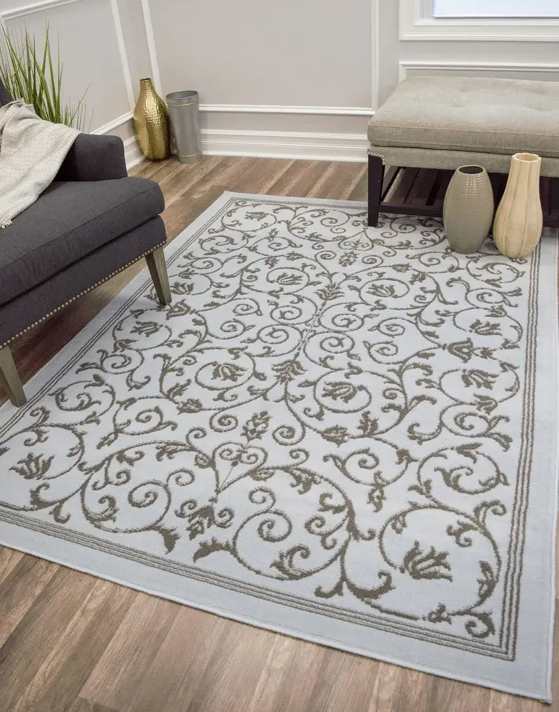 White rug with a brown floral scroll pattern in a living room featuring a gray chair, bench, and decorative vases.