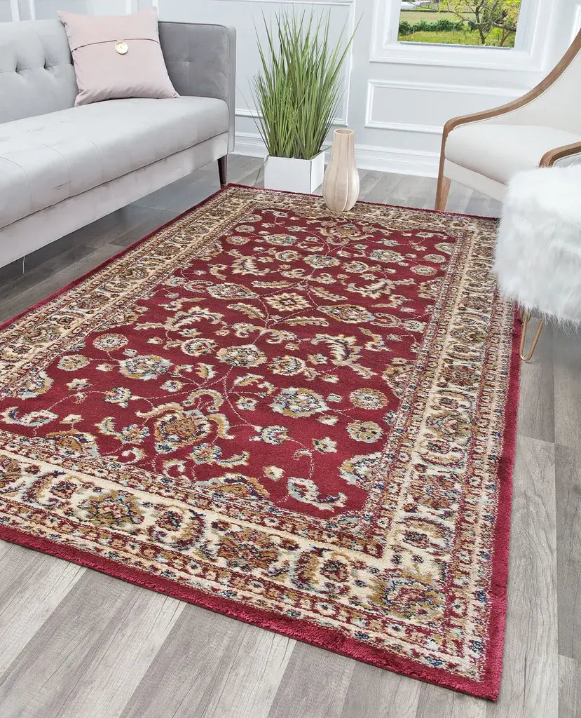 Rich red rug with intricate designs in a living room featuring a grey sofa, pink pillows, a potted plant, and a wooden chair