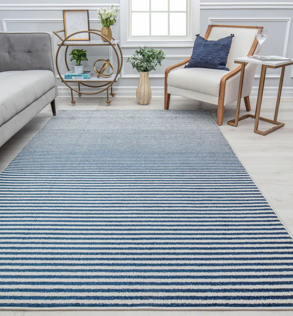 Contemporary striped rug in shades of blue and white, placed in a cozy living room with a gray sofa, wooden chair, and decor accents.