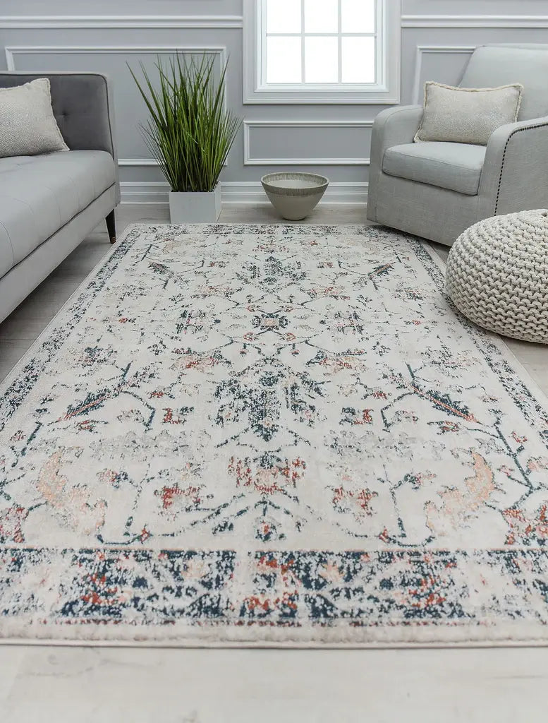 Modern living room featuring a light-colored floral rug, gray sofas, a knitted pouf, green plant, and decorative bowl