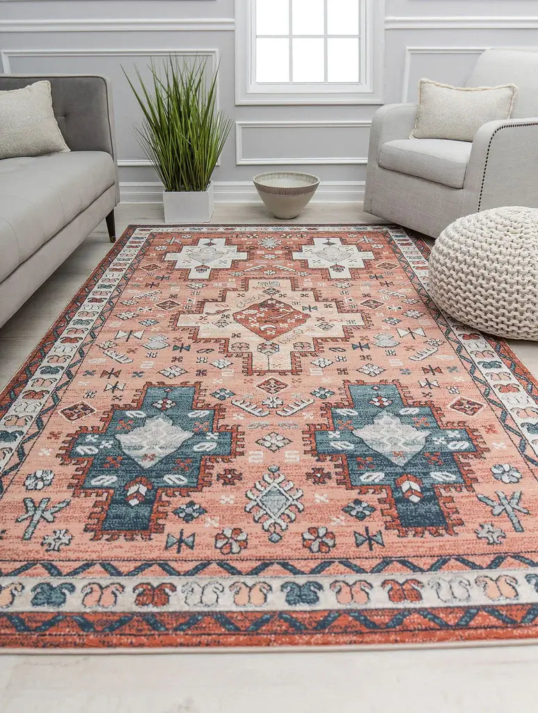 Peach and blue rug with geometric patterns in a light living room with gray and white seating, a pouf, and potted plant.